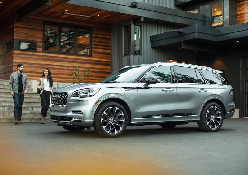 A couple approach a 2023 Lincoln Aviator® Grand Touring model parked in the driveway of a modern home | Green Lincoln in Greensboro NC