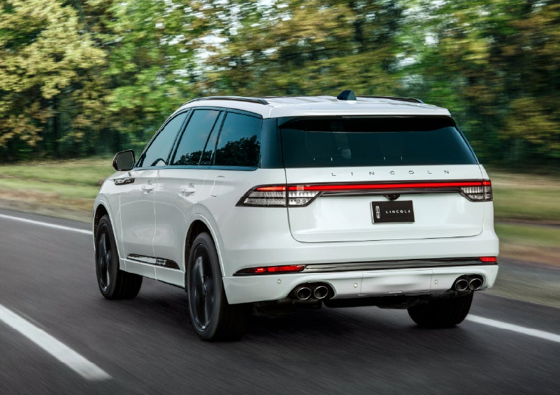 A white 2026 Lincoln Aviator® SUV is being driven away down a road lined with colorful trees. | Green Lincoln in Greensboro NC