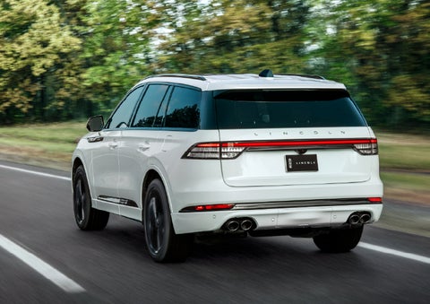 A white 2026 Lincoln Aviator® SUV is being driven away down a road lined with colorful trees. | Green Lincoln in Greensboro NC