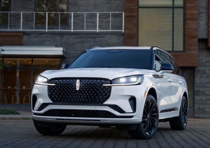 A 2026 Lincoln Aviator® Reserve model is shown with the available Jet Appearance Package parked near a restaurant. | Green Lincoln in Greensboro NC