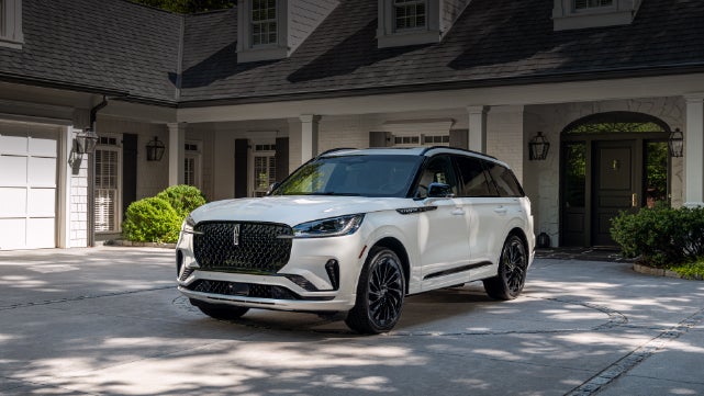 A white 2026 Lincoln Aviator® SUV is parked in the driveway of a luxury home. | Green Lincoln in Greensboro NC