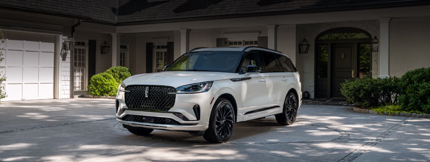 A white 2026 Lincoln Aviator® SUV is parked in the driveway of a luxury home. | Green Lincoln in Greensboro NC