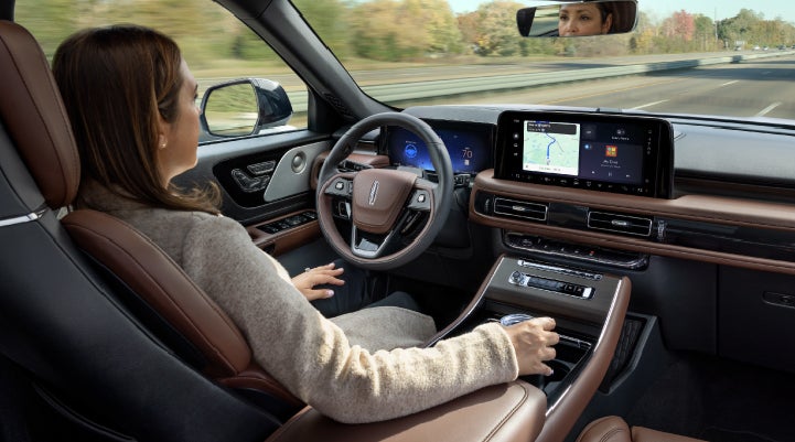 A 2027 Lincoln Aviator® SUV is being driven hands-free on a highway lined with trees. | Green Lincoln in Greensboro NC