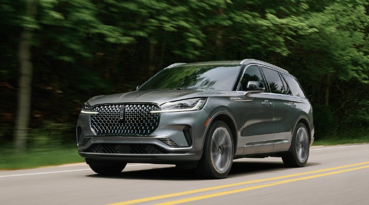 A 2027 Lincoln Aviator® SUV is being driven down a road lined with trees. | Green Lincoln in Greensboro NC