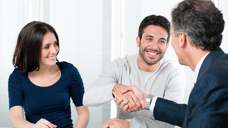 A smiling couple shaking hands with a professional in an office setting.