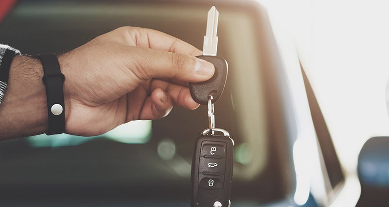 Hand holding car keys with a car interior blurred in the background.
